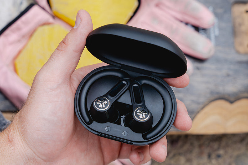 Black wireless earbuds in a case held by a hand with a blurred background