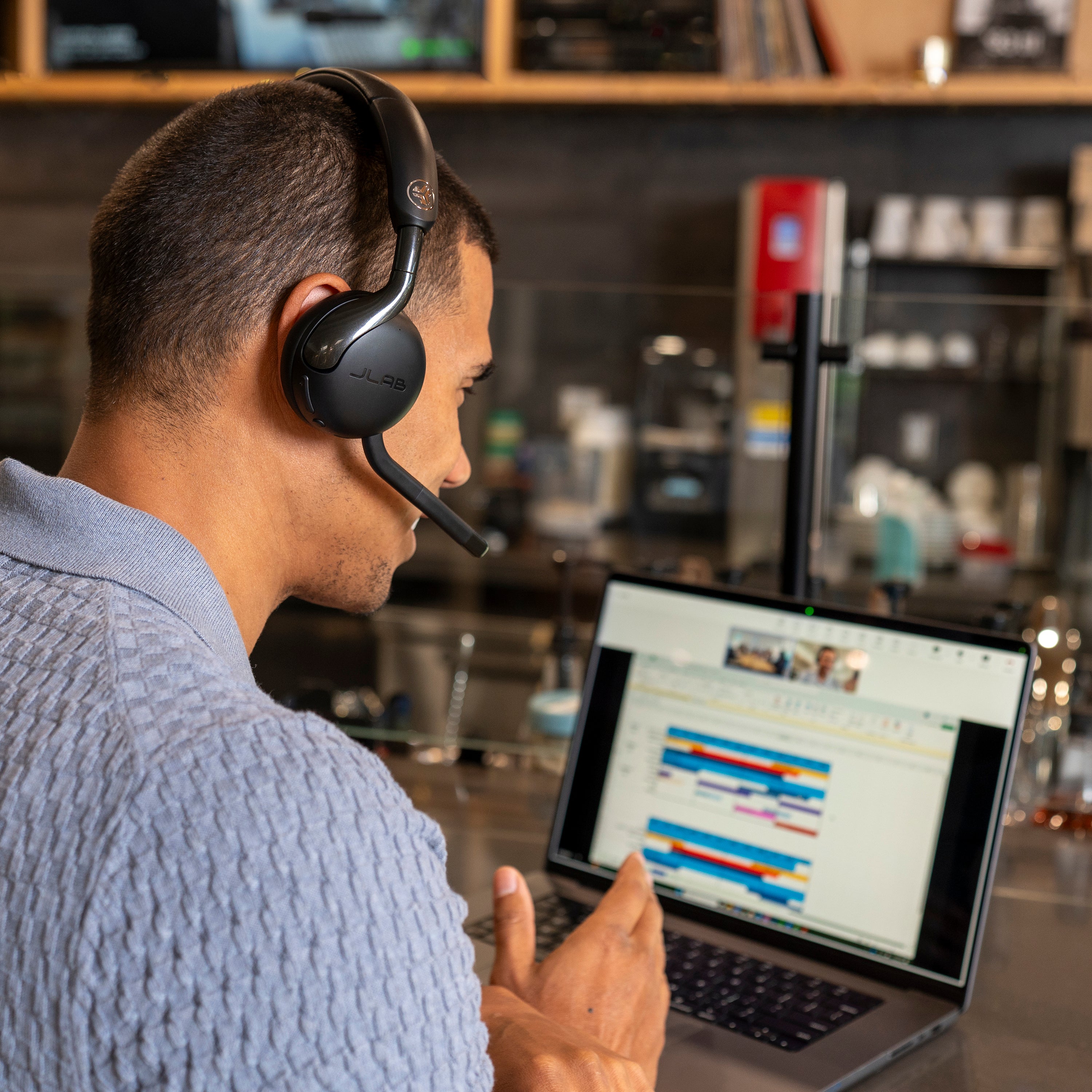 Person wearing a headset using a laptop in a coffee shop setting