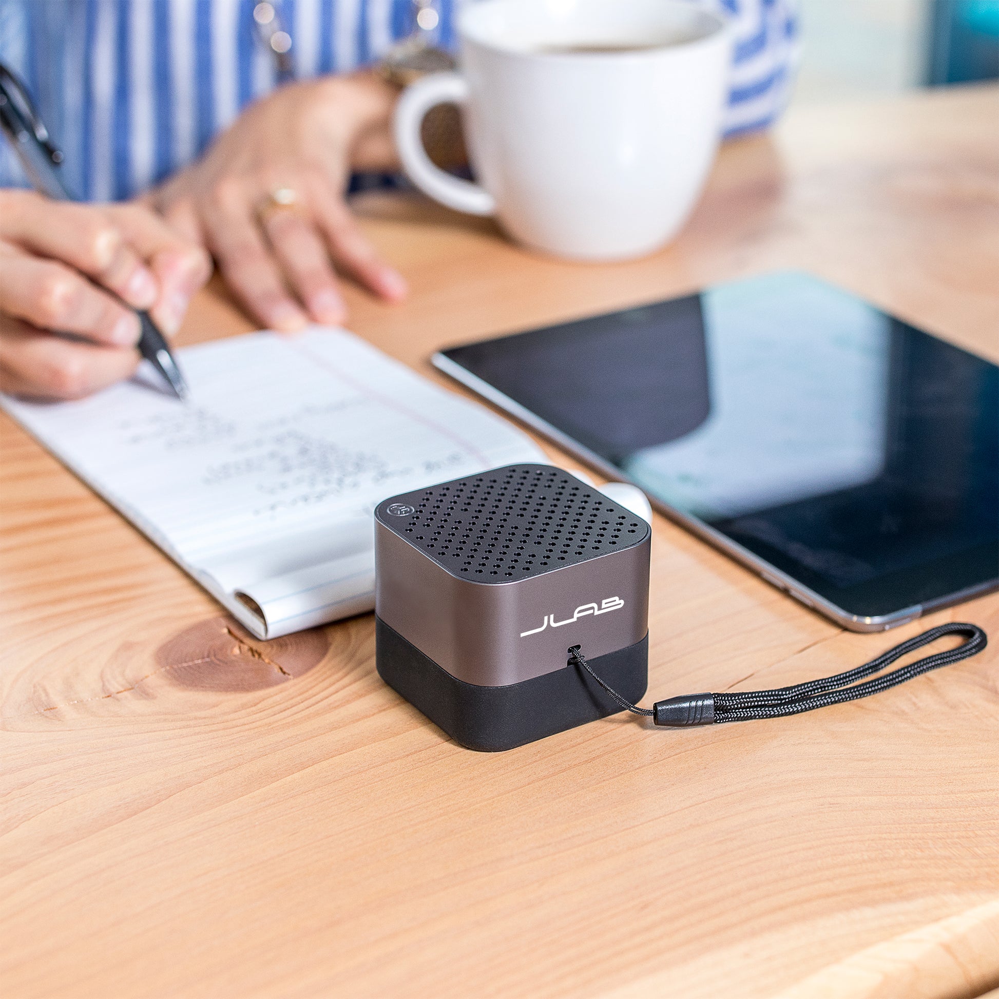 Gunmetal Crasher Micro Speaker on Desk Next to Woman Writing